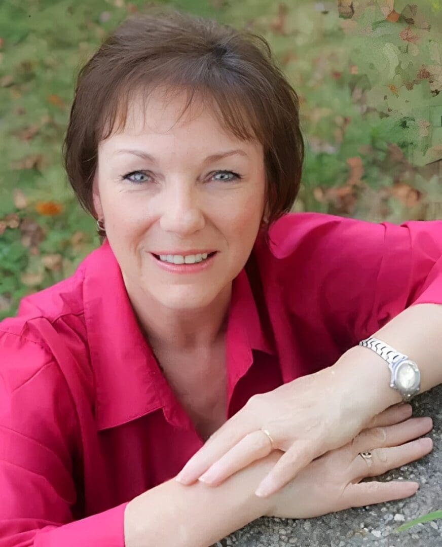 A woman in pink shirt sitting on ground with her hands crossed.
